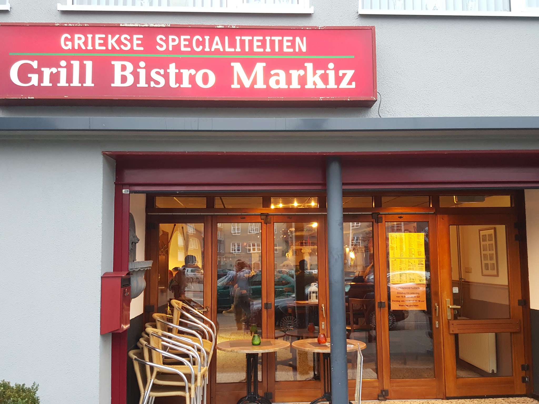 De voorgevel van Grill-bistro Markiz aan de Zonstraat in de avond, met verlichte naam en terrasstoelen